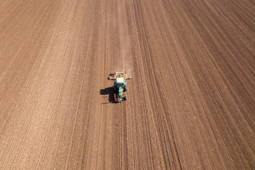 Green Tractor cultivating and seeding a dry field - Top down aerial image
