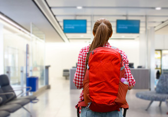 travel, tourism and people concept - young woman with red backpack over airport terminal background