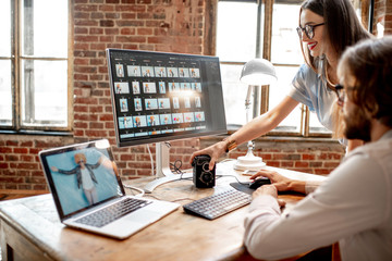 Young couple of photographers working with woman's portraits at the working place with two...