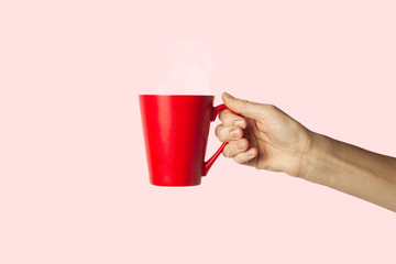 Female hand holding a red cup with hot coffee on a pink background. Side view