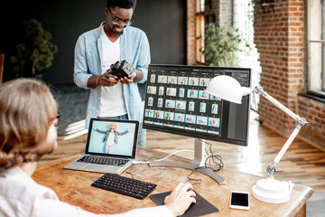 Two male photographers choosing woman's portraits at the working place with two computers in the...