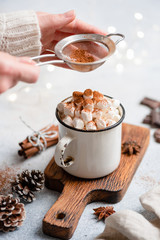 Hot chocolate with marshmallows in mug. Sifting cocoa powder over hot chocolate drink with marshmallows