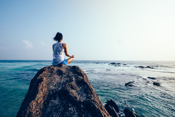 Young woman meditation on seaside rock cliff edge