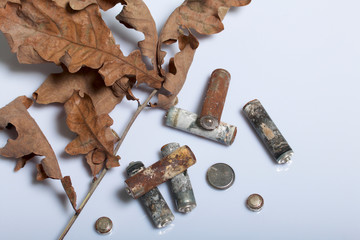 Spent batteries, coated with corrosion. Different shapes and sizes. They lie on a white background among the dead autumn leaves. Environmental protection, recycling.