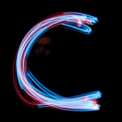 Letter С of the alphabet made from neon sign. The blue light image, long exposure with colored fairy lights, against a black background