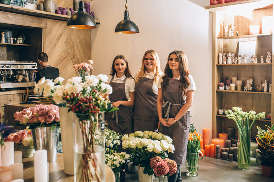 Full length of three female florists team standing alongside in floral shop with flowers in pots around. Small business, welcoming concept.