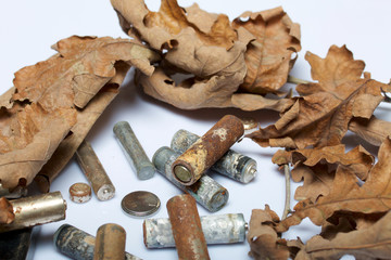 Spent batteries, coated with corrosion. Different shapes and sizes. They lie on a white background among the dead autumn leaves. Environmental protection, recycling.