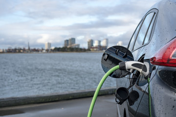 Charging an electric car, with the city and water in the background, green charging cable and black...