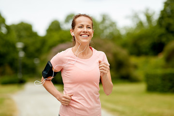 fitness, sport and healthy lifestyle concept - smiling woman with earphones wearing armband for...