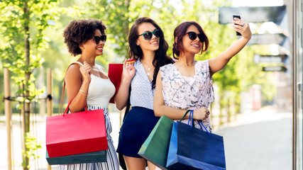 sale, consumerism and technology concept - happy young women with shopping bags taking selfie by smartphone in city