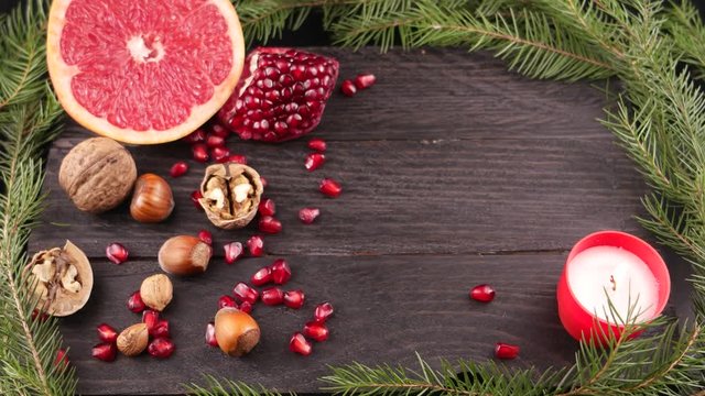 Still life with a burning candle, half grapefruit, pine branch, pomegranate and nuts on the brown wooden board