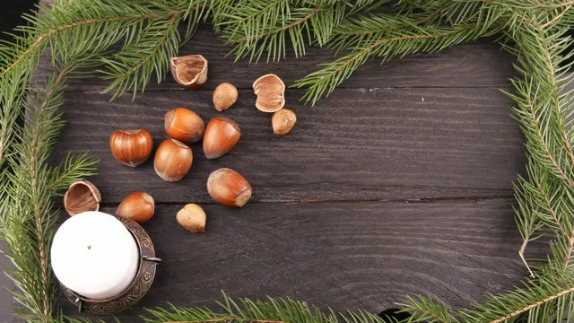 Still life with a burning candle, pine branch and hazelnuts on the brown wooden board
