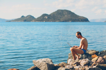Young man freelancer works with a laptop by the sea