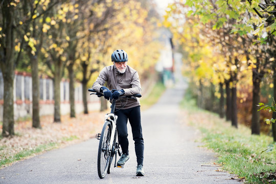 Active senior man with electrobike standing outdoors on a road in nature.
