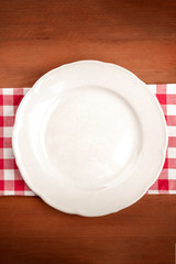 A photo of a white plate on a vichy table cloth on a dark rustic wooden background with a place for text