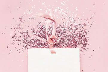 Flat lay top view White gift bag and holographic glitter confetti in the form of stars on pink...