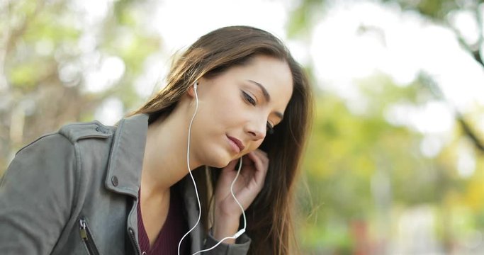 Relaxed woman putting earbuds on ears and listening to music from a smart phone in a park