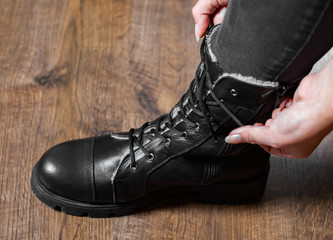 Tying Shoes on wooden floor, women fashion black leather boots.