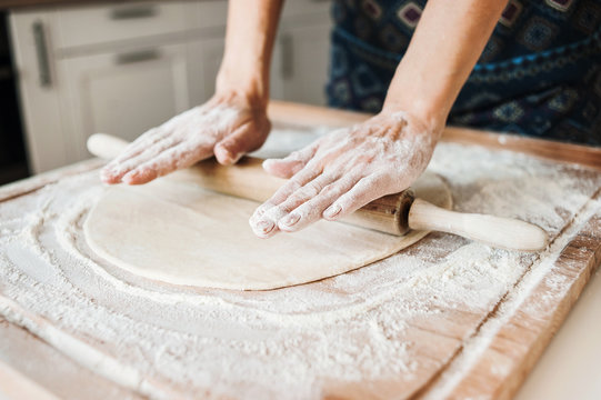 Woman baking bread or pizza dough with rolling pin on wooden table. Preparing dough