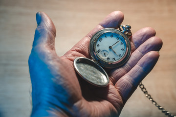 old man holds in his hand a retro pocket watch on a chain, the concept of a bygone time and old age