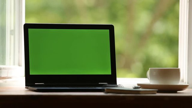 Laptop with track green screen on a desktop there is a hot steaming cup of tea