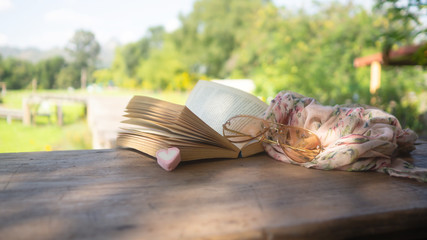 Old book,  Flower scarf and glasses All set on a wooden table In the garden.