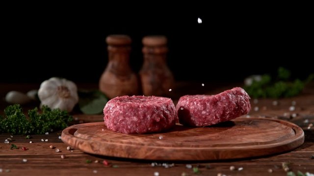 Super slowmotion footage of strewing salt and pepper at fresh raw beef meat burger, 1000fps, 4K