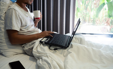 Asian business man have beard siting in the bed in the morning, Work on  notebook in his lap, at the same time drink coffee, Concept working on the bed.