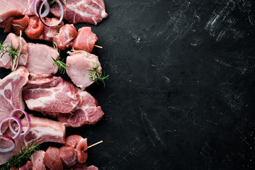 Raw meat for barbecue. Meat with spices and herbs. On a black stone background. Top view. Free copy space.