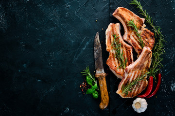 Steaks on the bone with rosemary. Grill, barbecue. On a black stone background. Top view. Free copy...