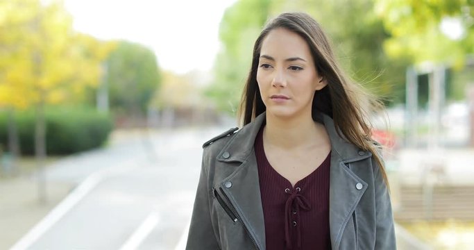 Front view of a serious pensive woman walking towards camera looking at side in a park