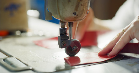 Close up of a shoemaker sewing a red leather by using a sewing machine according to the italian...