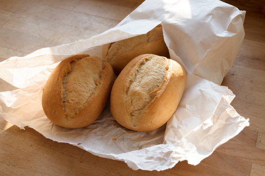 fresh bread rolls or buns from the bakery in a white paper bag on a wooden table