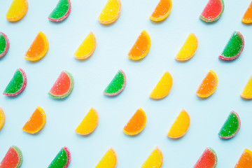 Slices of colorful candied fruit jelly on light pastel blue background. Sweets pattern. Top view.