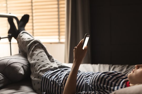 Woman using mobile phone on bed in bedroom