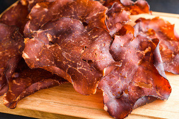 Thinly sliced and dried smoked ham on oak tray. Small crystals of salt visible on the meat.