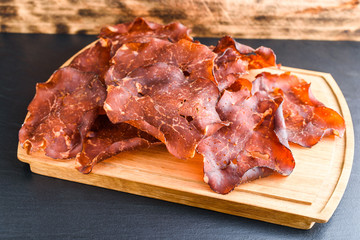 Thinly sliced and dried smoked ham on oak tray. Small crystals of salt visible on the meat.