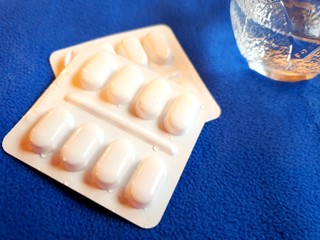 Pills and glass of water on blue background with copy space