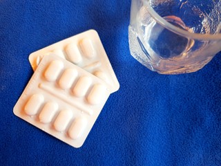 Pills and glass of water on blue background with copy space