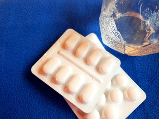 Pills and glass of water on blue background with copy space