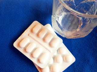 Pills and glass of water on blue background with copy space