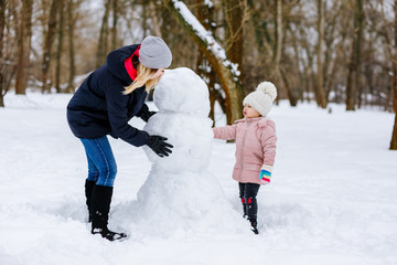 Fototapeta na wymiar mom and daughter make a snowman out of snow