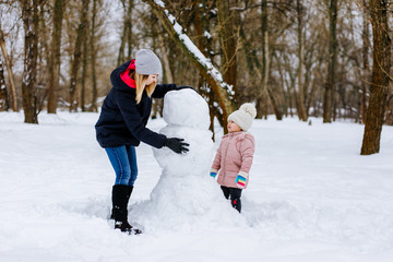 mom and daughter make a snowman out of snow