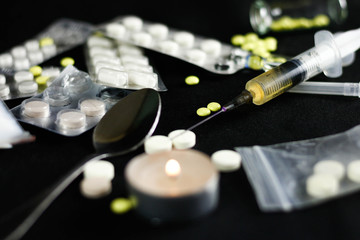 Drugs on a black background. Syringe, needle, pills, white powder, candle, spoon. Close up.