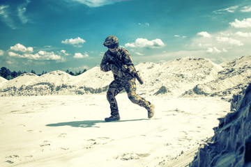 Man in military camouflage uniform with airsoft weapon bending down and running during armed...