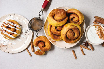 Homemade pumpkin cinnamon bun rolls sweet autumn baked dessert with cream cheese sauce in spotted...