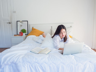 asian woman using computer and read book on bed in the morning
