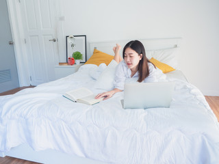 Obraz na płótnie Canvas asian woman using computer and read book on bed in the morning