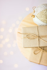 Christmas gift boxes wrapped in craft paper tied with twine hand crafted linen fabric ornament ball on wooden stool. Golden garland bokeh lights. Holiday preparation concept. New Year