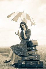 Young beautiful adult girl with suitcases and umbrella on rural road during travelling. Image in...